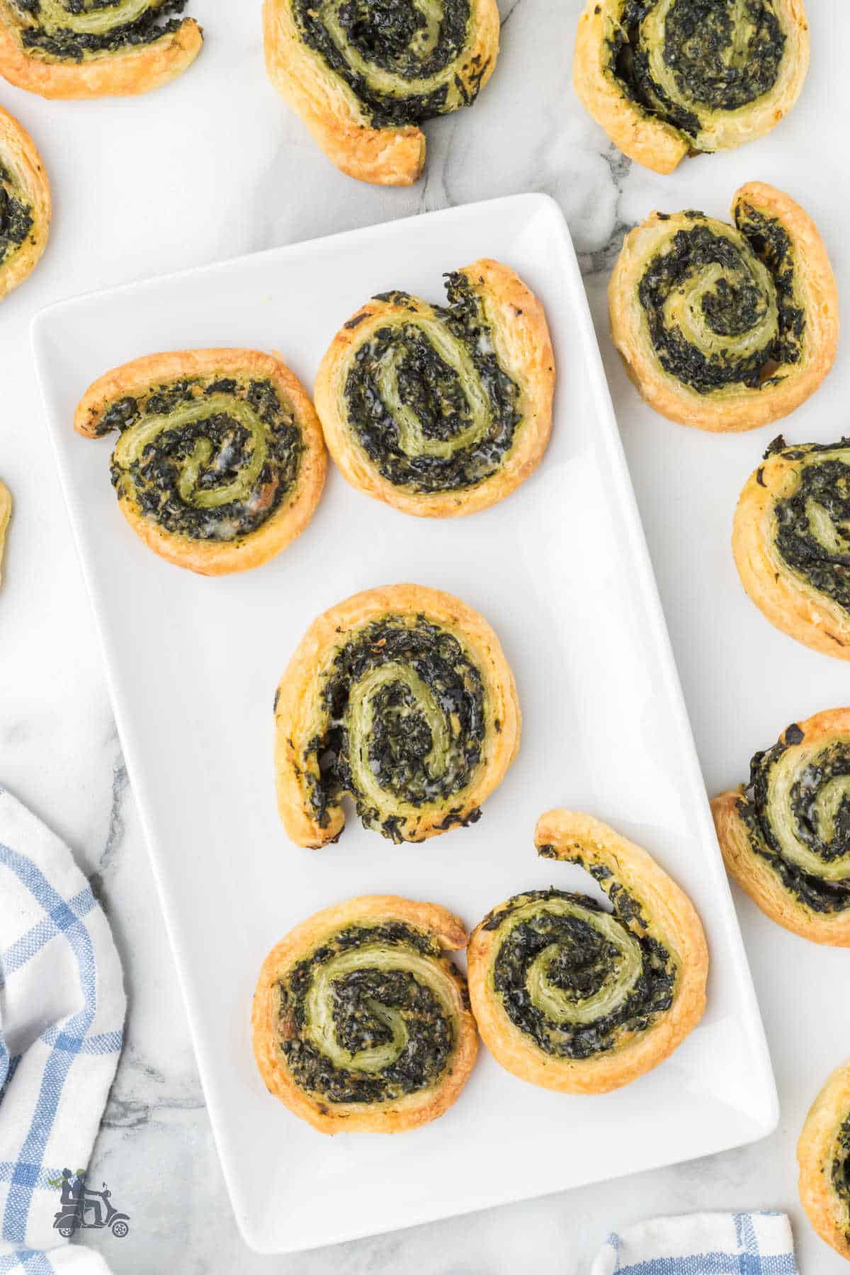 Overhead view of the spinach puff pastry appetizers on a white serving plate with more appetizers surrounding it. 