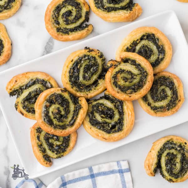 The cream cheese puff pastry appetizers on a serving plate with several appetizers on the table.
