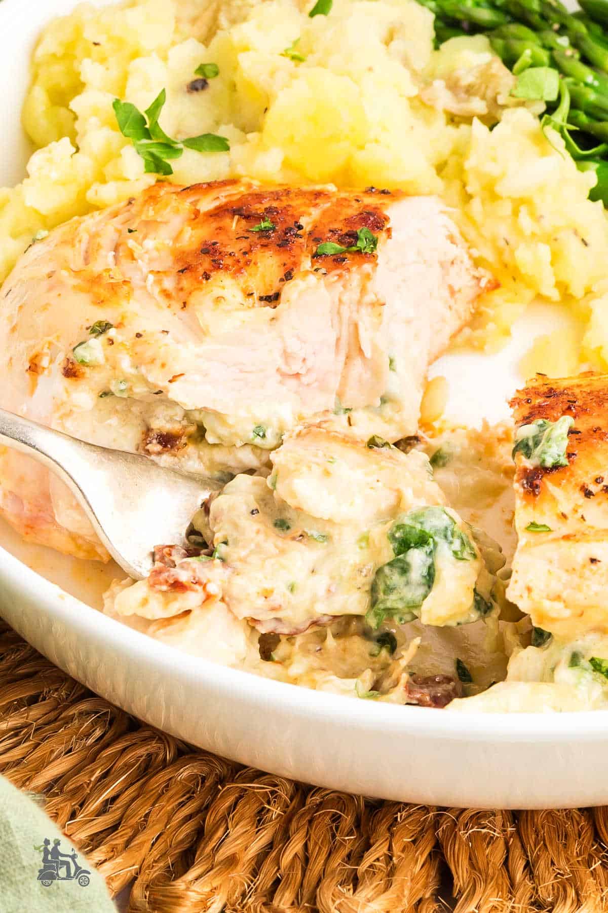 A closeup of a fork cutting into the juicy stuffed chicken breasts with sun-dried tomatoes on a plate.