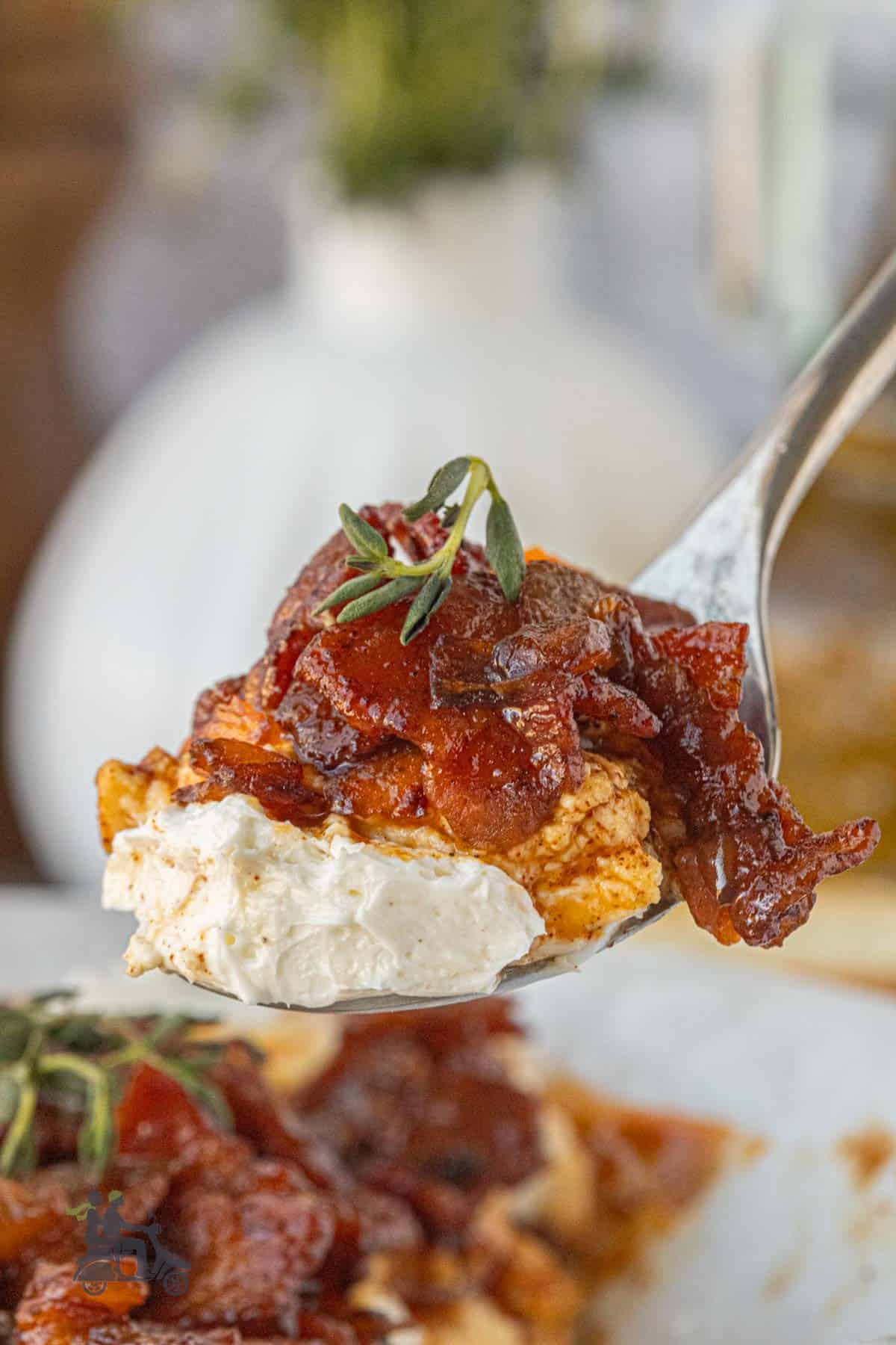 Close-up of a spoon holding sweet and smoky bacon jam layered over whipped goat cheese.