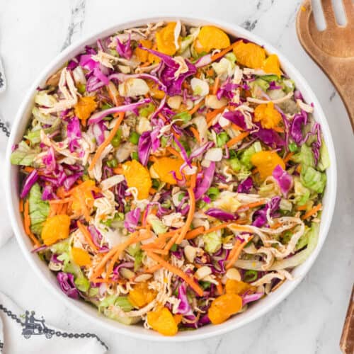 Salad bowl filled with mandarin orange chicken salad topped with sliced almonds, green onions, and mixed with crunchy ramen noodles.