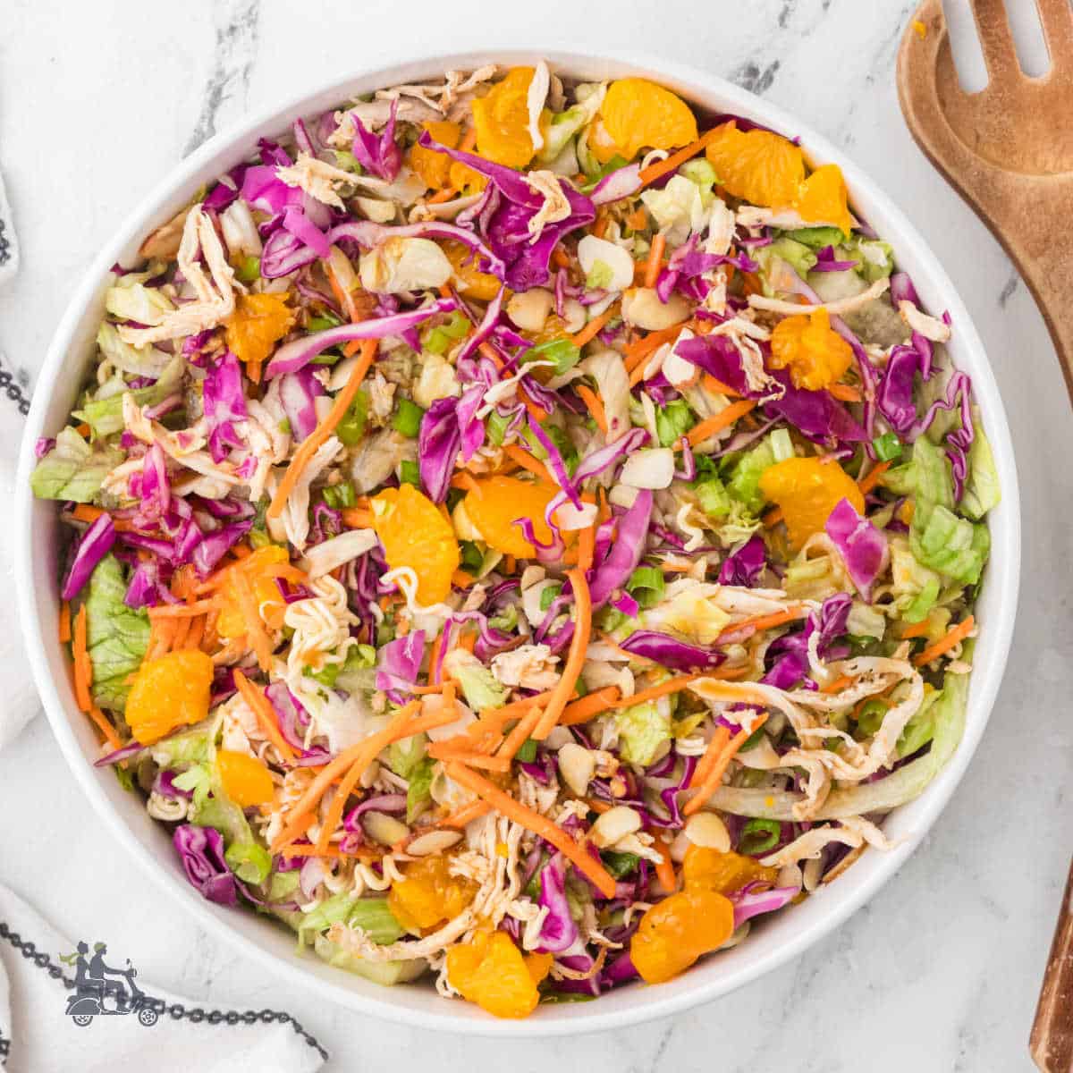 Salad bowl filled with mandarin orange chicken salad topped with sliced almonds, green onions, and mixed with crunchy ramen noodles.