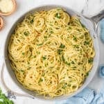 Spaghetti aglio olio and peperoncini in a skillet with flat-leaf parsley and parmesan sprinkled on top.