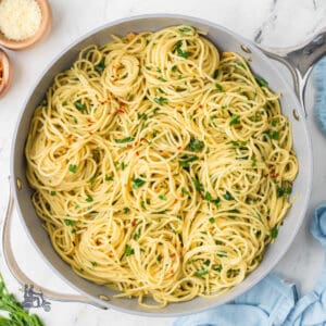 Spaghetti aglio olio and peperoncini in a skillet with flat-leaf parsley and parmesan sprinkled on top.