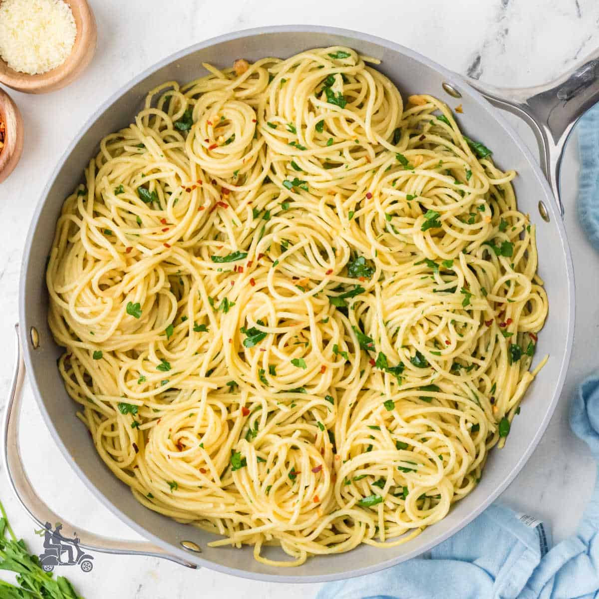 Spaghetti aglio olio and peperoncini in a skillet with flat-leaf parsley and parmesan sprinkled on top.
