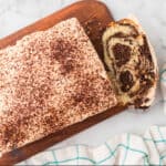 Tiramisu Quick Bread with Mascarpone frosting on a cutting board with a bread slice showing.