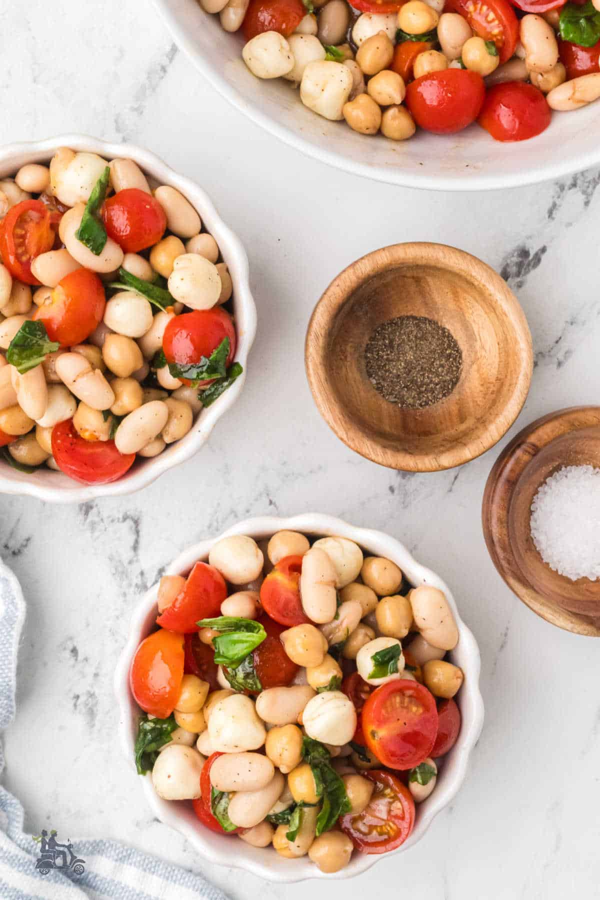 Caprese Dense Bean Salad with chickpeas, canneliini beans, cherry tomatoes, mozzarella pearls, and fresh basil tossed with a vinaigrette dressing.
