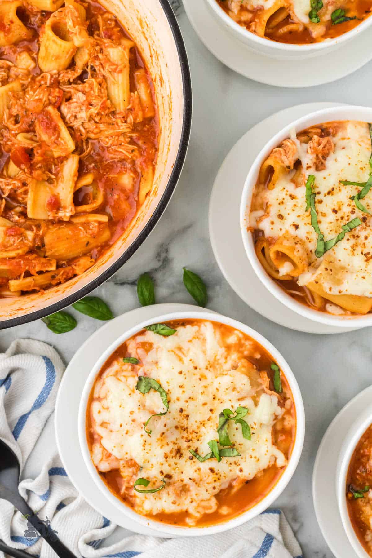 Italian inspired Parmesan Chicken Soup in white bowls with Dutch oven off to the side.