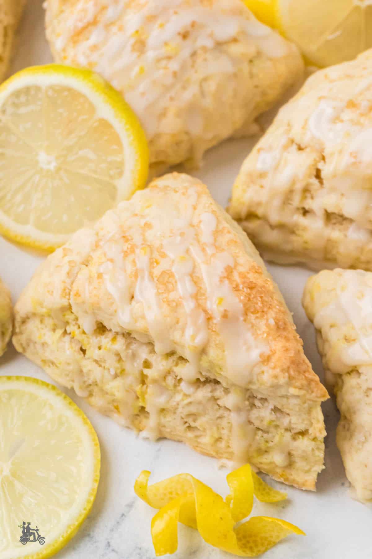 Buttermilk lemon scones with lemon glaze on a white counter with fresh lemon slices.