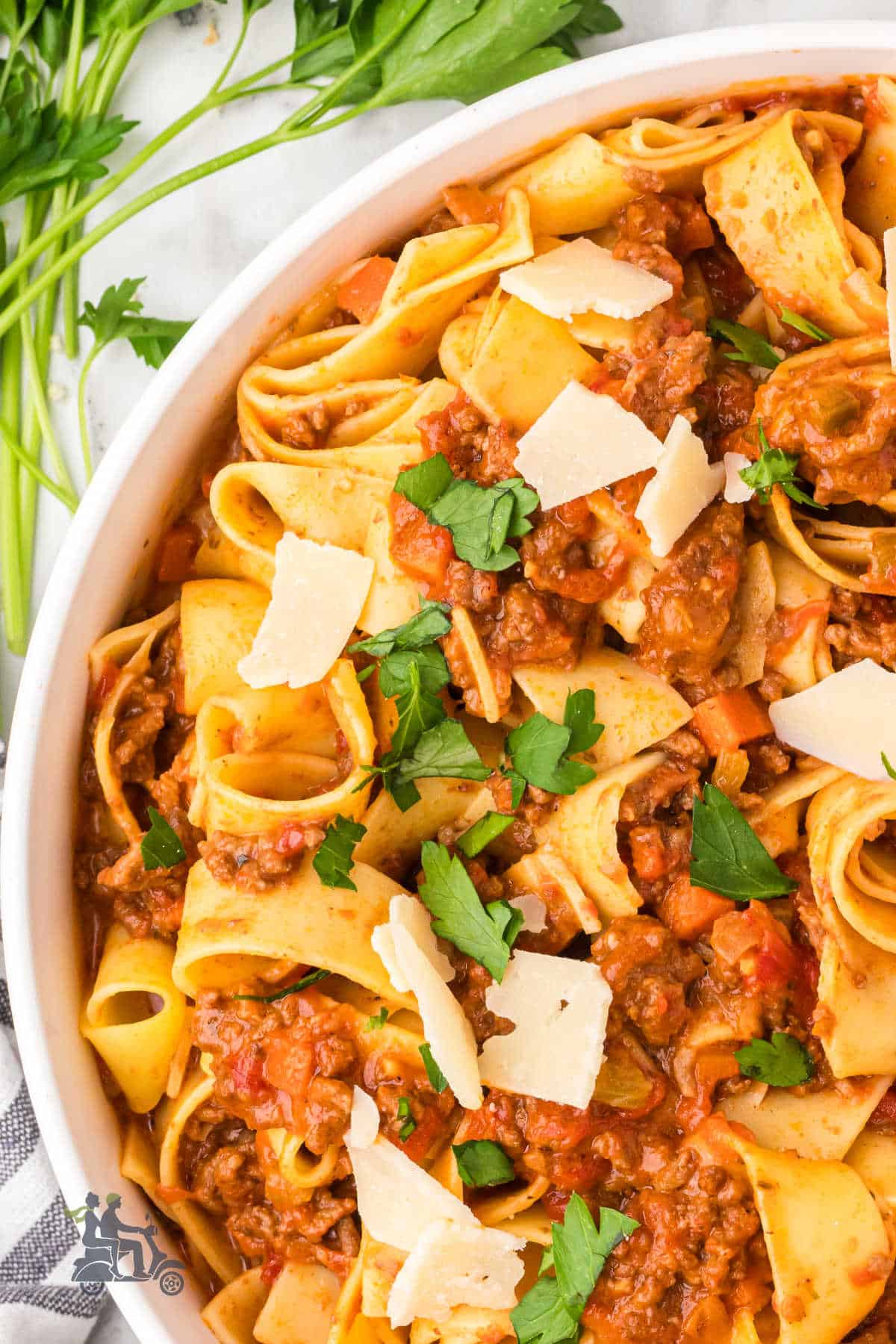 A tight close-up shows silky pappardelle coated in rich Bolognese sauce. It’s finished with a pinch of parsley and a snowfall of grated Parmigiano-Reggiano.