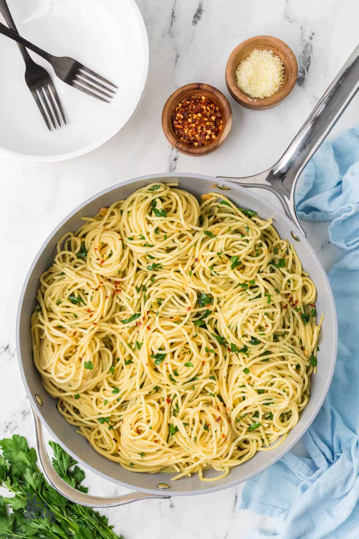 Skillet filled with spaghetti made with aglio, olio with peperoncini and topped with flat-leaf parsley and Parmesan cheese. 