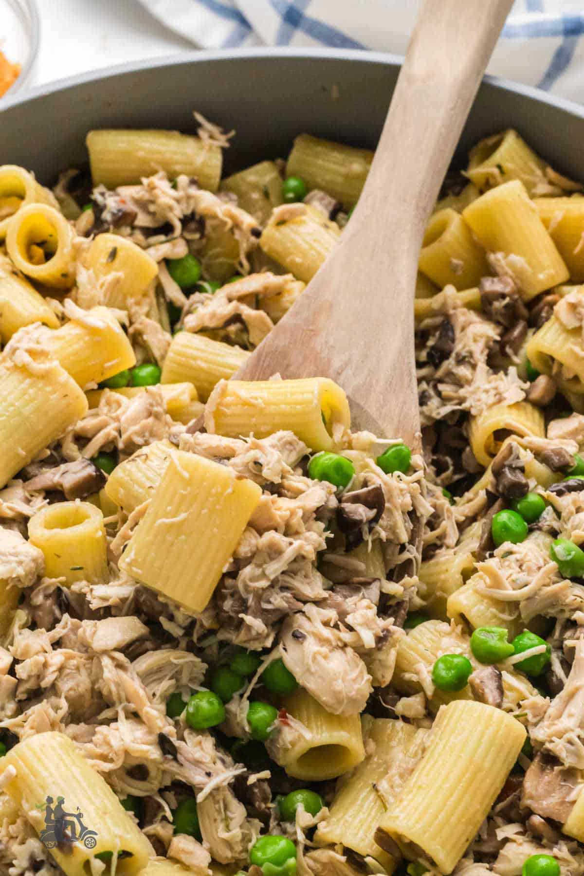Close-up of a wooden spoon scooping up a helping of the creamy rotini with diced rotisserie chicken and peas.