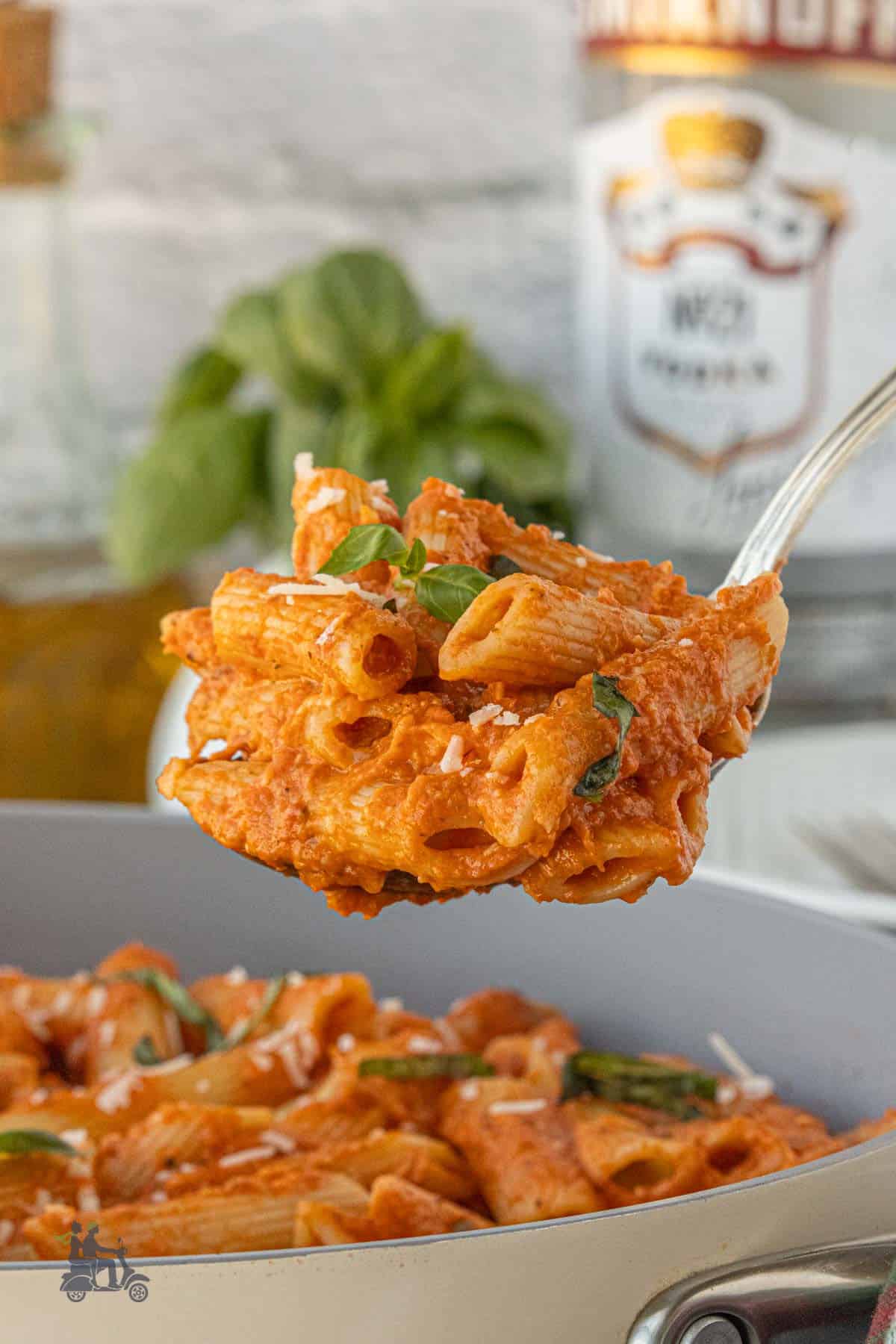 Serving spoon lifting a helping of penne pasta mixed with oven-roasted tomato vodka sauce.