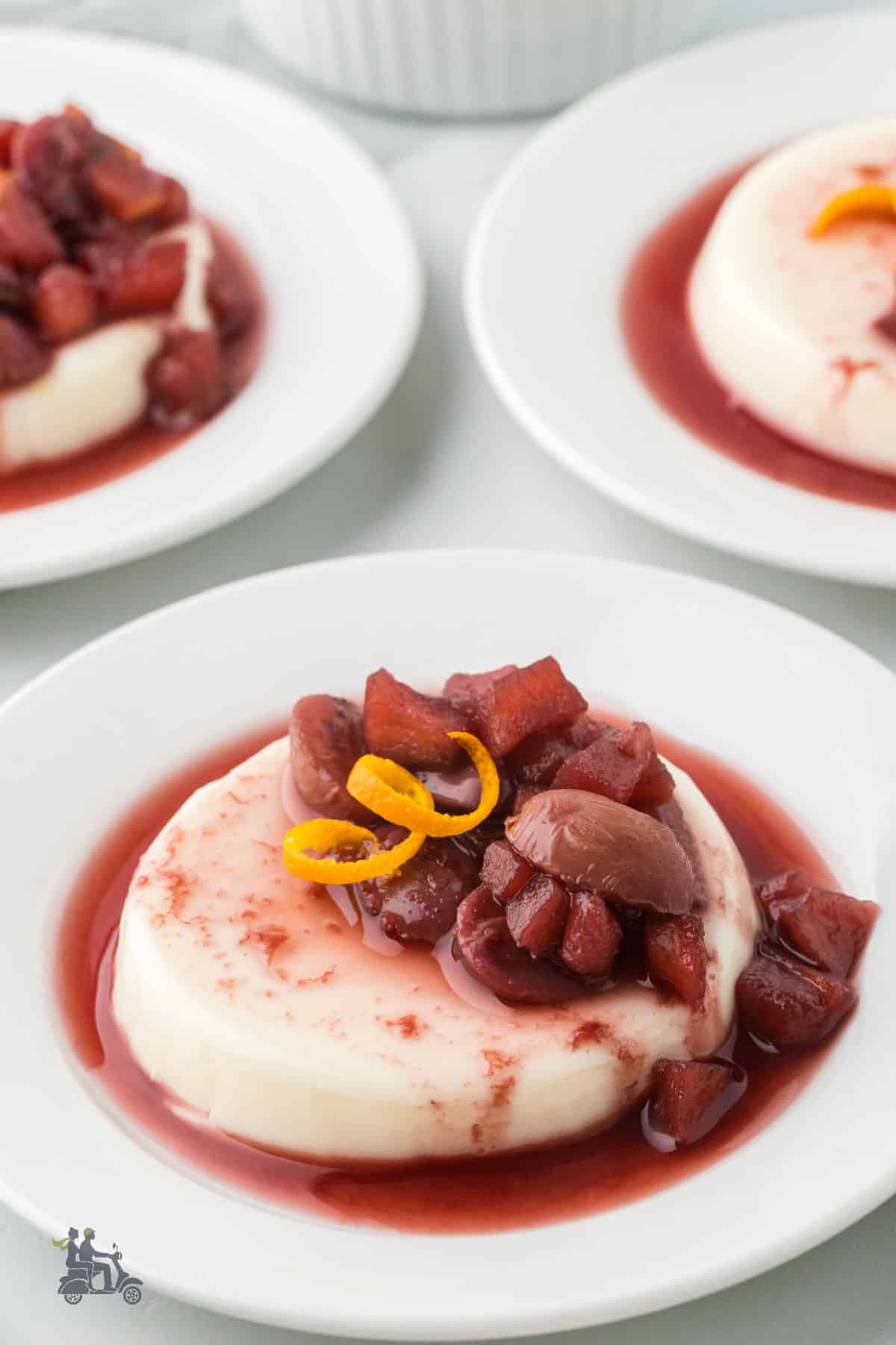 Ruby port fruit sauce spooned over chilled panna cotta on a dessert plate.