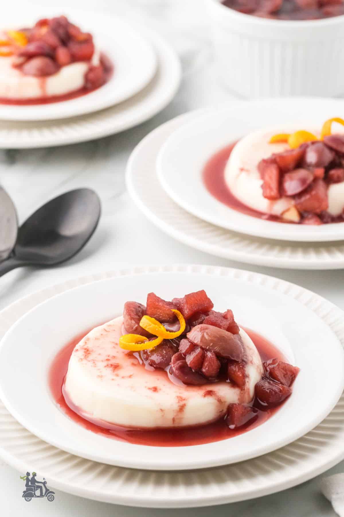 Buttermilk panna cotta on a dessert plate topped with apples, pears, and grapes in ruby port sauce