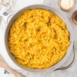 Saucepan filled with golden butternut squash orzo risotto seasoned with sage and Parmesan cheese.