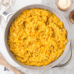 Saucepan filled with golden butternut squash orzo risotto seasoned with sage and Parmesan cheese.