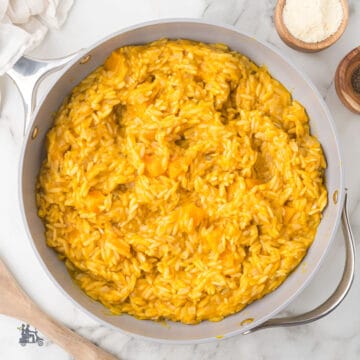 Saucepan filled with golden butternut squash orzo risotto seasoned with sage and Parmesan cheese.