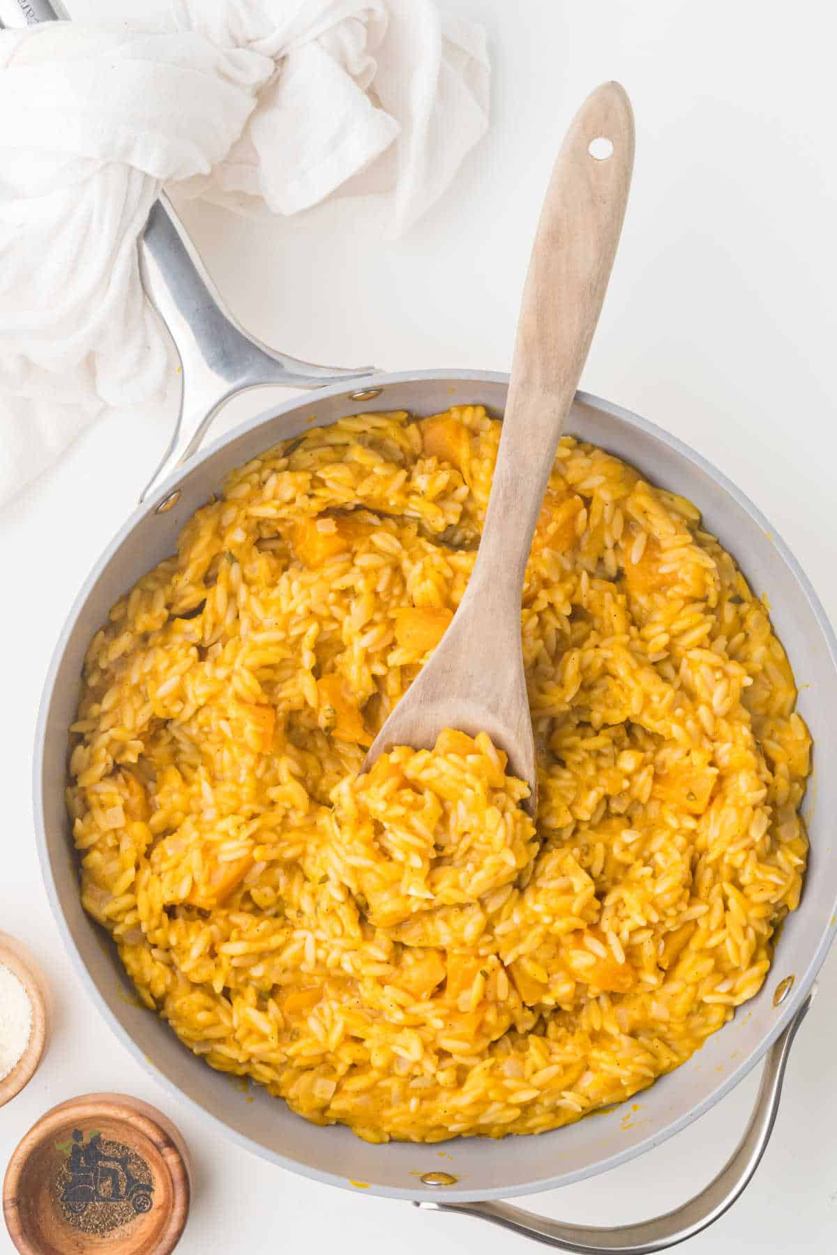 Butternut squash risotto topped with grated Parmesan cheese and sprinkled with black pepper in skillet with wooden spoon. 
