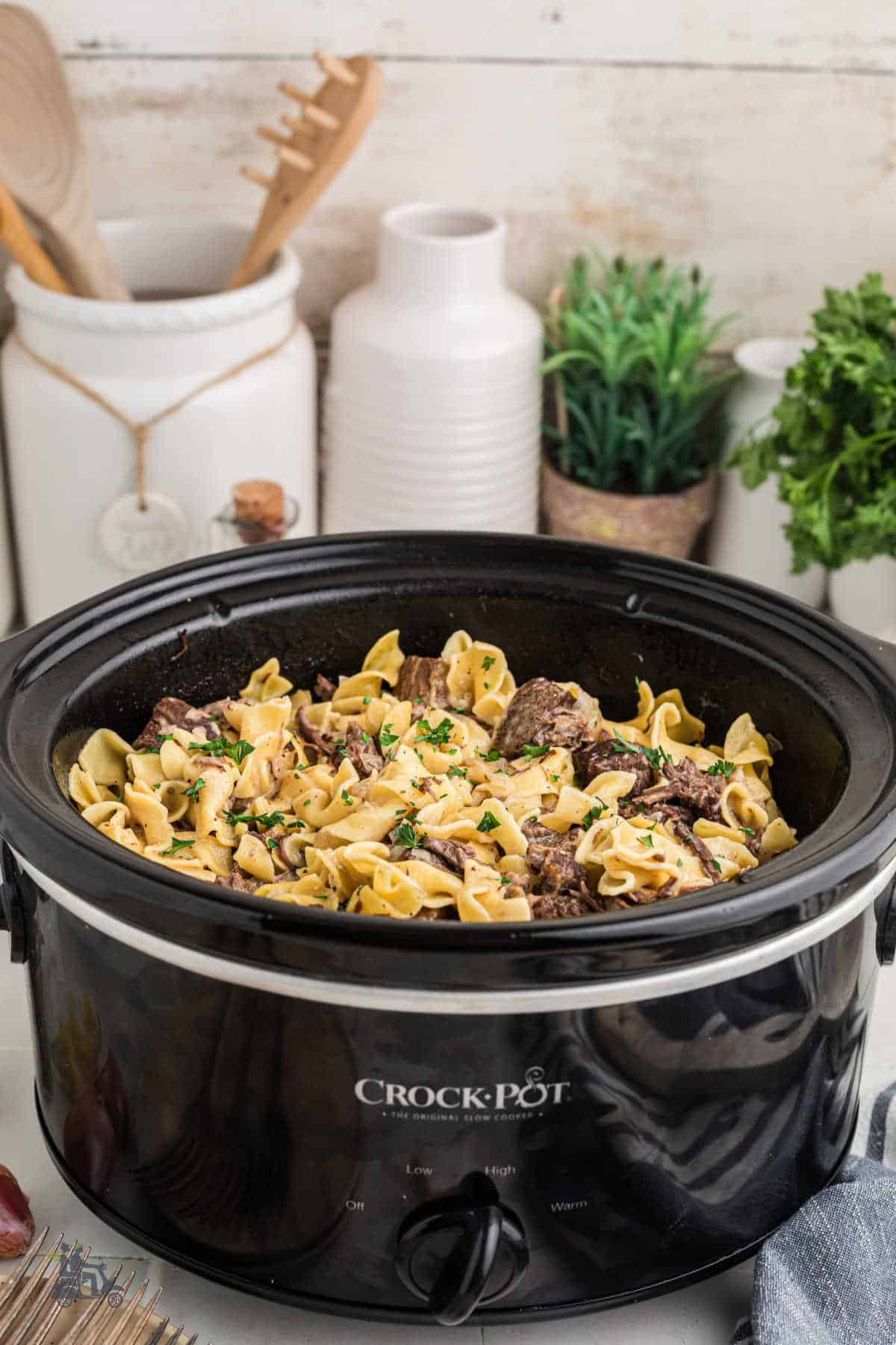 A black crockpot is filled with the finished seasoned beef and noodles comfort recipe.
