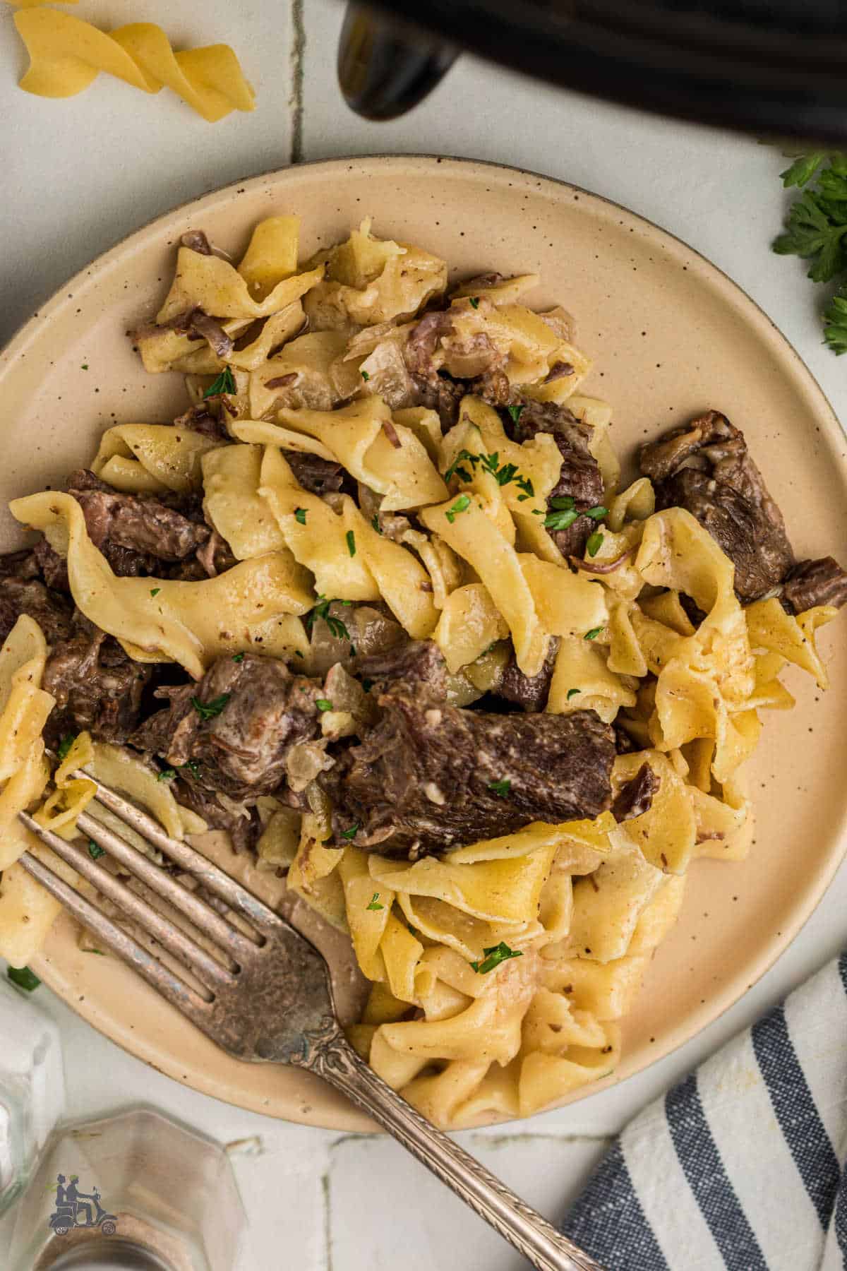 A white plate with fork holds a serving of tender beef and egg noodles coated in creamy beef gravy.