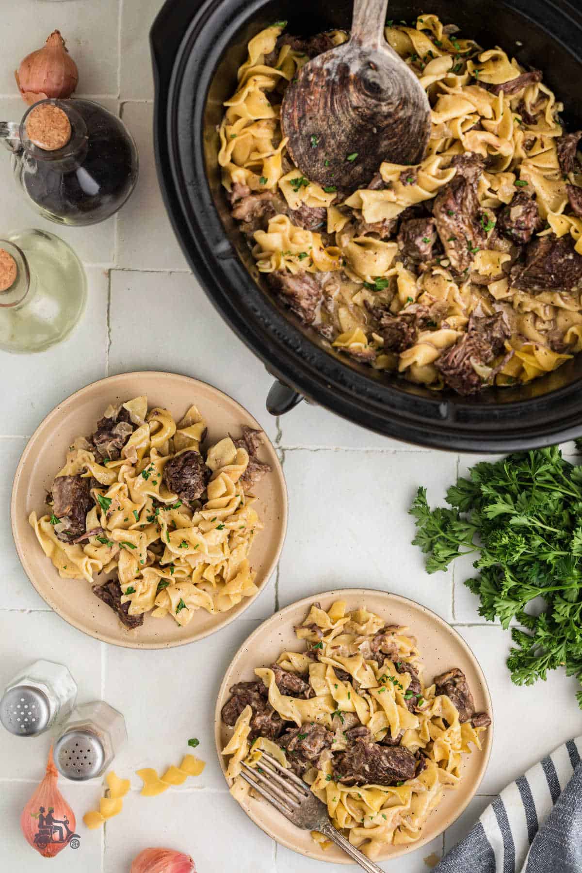 Overhead view of the finished seasoned cubed beef and egg pasta recipe on serving plates with the slow cooker in the background.
