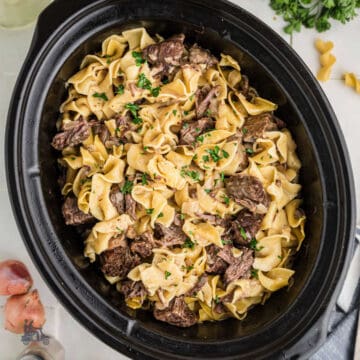 Slow cooker beef and noodles with chunks of chuck roast and extra-wide egg noodles in a crockpot.